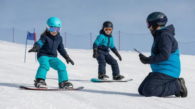 Karlı alanda snowboardlar üzerinde iki çocuk; sağda panoya bakan diz çökmüş yetişkin