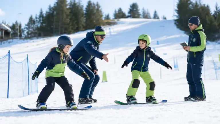 Karlı alanda snowboardlar üzerinde iki çocuk; ortada eliyle işaret eden ve sağda tablet tutan iki yetişkin